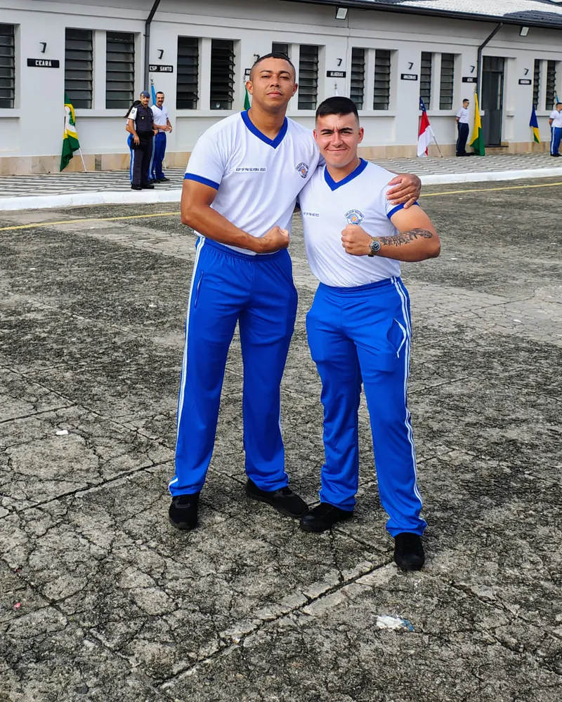 Dois rapazes de uniforme de educação física da PM, abraçados em frente ao prédio do comando
