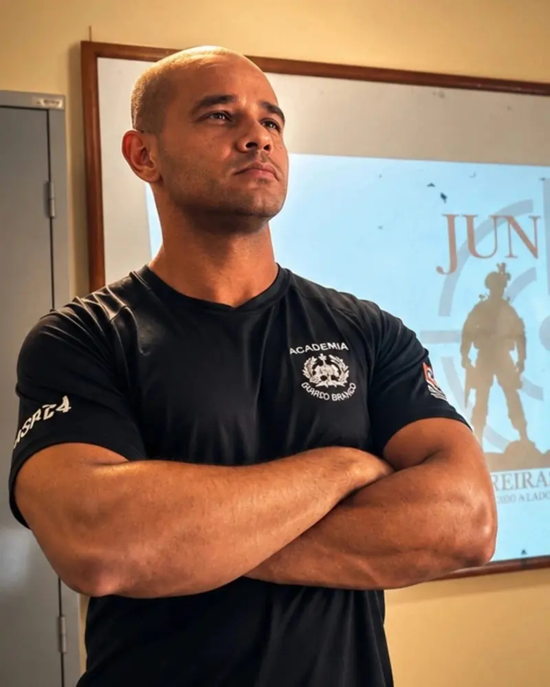 Kilder de braços cruzados, de camiseta preta da academia, em frente ao slide do Juntos Carreiras Policiais